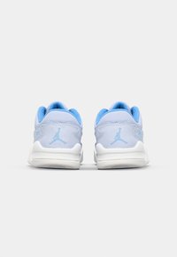 Une paire de baskets bleu clair et blanches avec un logo Jumpman bleu sur le talon, vue de dos sur un fond blanc uni.