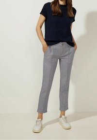 Námořnický top s krátkým rukávem, vzorované světle modré a bílé kostkované kalhoty a bílé tenisky. Kalhoty mají přední kapsy a knoflík.