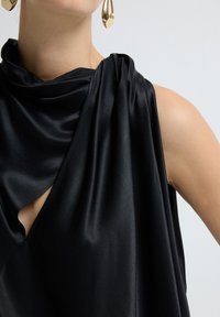 Zwarte satijnen top met een cowl neck en asymmetrische snit, met een kleine opening en een gladde textuur. Vergezeld van gouden accessoires.