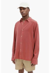 Rustfarvet skjorte med knapper og en blød tekstur, lange ærmer og klassisk krave, sammen med beige shorts.