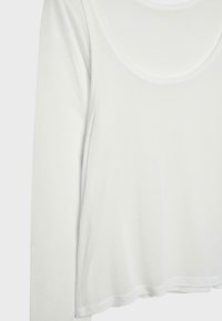 Biela dlhá košeľa s okrúhlym výstrihom, mäkkou tkaninou a jemne zaobleným lemom, zobrazená na čistom pozadí.