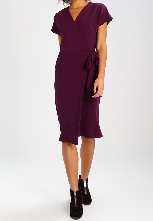Vestito avvolgente prugna con maniche corte, cintura legata in vita e orlo asimmetrico. Indossato con stivali neri alla caviglia con cerniere. Texture liscia.