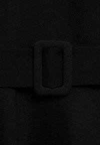Ceinture en tissu noir avec une boucle rectangulaire recouverte de tissu, portée sur un vêtement texturé en tissu noir.