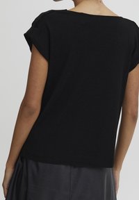 Zwart T-shirt met korte mouwen dat een losse pasvorm, een gladde textuur en een brede halslijn heeft, weergegeven vanuit een achteraanzicht.