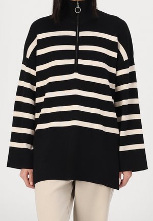 Pull à manches longues rayé noir et beige avec col montant et demi-fermeture éclair avec une tirette ronde.