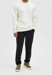 Ljusbeige sweatshirt med bröstficka, tillsammans med mörkblå sweatpants och bruna sneakers. Avslappnad outfit med minimalistisk design.