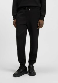 Black jogger pants with an elastic waistband, drawstring closure, side pockets, and ribbed cuffs, made of soft, smooth fabric.