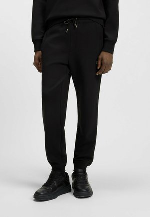 Black jogger pants with an elastic waistband, drawstring closure, side pockets, and ribbed cuffs, made of soft, smooth fabric.