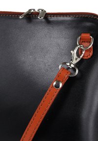 Schwarze Ledertasche mit glatter Textur, ausgestattet mit einem abnehmbaren orangen Riemen, silberner Beschläge und einem Reißverschluss oben.