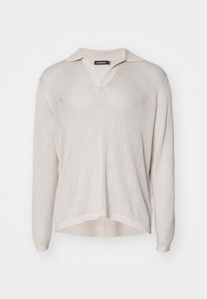 Kortermet, lys beige strikket genser med V-hals og krage. Har ribbestruktur og en avslappet passform med splitt i hemmet.