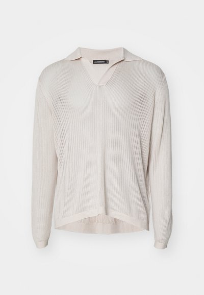 Pull à manches courtes en tricot léger beige clair, avec un col en V. Présente une texture côtelée et une coupe décontractée avec un ourlet fendu.