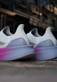 Sneakers bianchi dal design elegante, con una suola intermedia sfumata in rosa e grigio e una suola in gomma testurizzata. Gli accenti includono il branding.