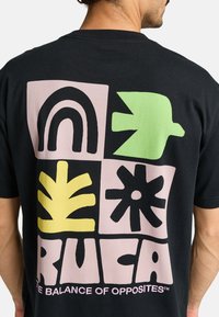 Zwarte t-shirt met een grafisch ontwerp bestaande uit zes vormen in pastelkleuren (roze, geel, groen) en dikke zwarte omtrekken. Afdruk op de bovenrug.