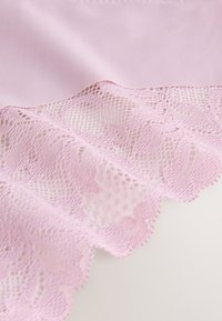 Hele roosa kangas pitsiservaga, mis kujutab keerukaid lillemotiive ja lainelisi ääri, pitsi kohal on sileda tekstuuriga kontrast.