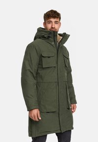 Parka verde oliva con chiusura a zip frontale, cappuccio regolabile e numerose tasche frontali. Presenta una finitura testurizzata e foderatura calda.