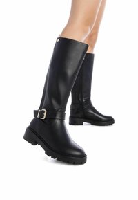 Botas de cuero negro hasta la rodilla con una suela gruesa, que cuentan con un cierre lateral, acento de hebilla y una textura suave.