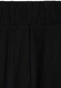 Gros plan d’un pantalon en tissu noir avec une ceinture élastique et un détail de couture verticale au centre avant.