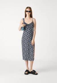 Navy blomstrete kjole med tynne stropper, med en frontsplitt. Kombinert med svarte platåsandaler og en liten blå håndveske.
