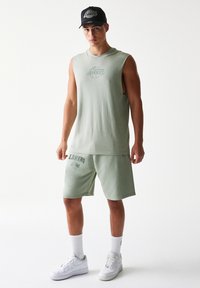 Αμάνικο ανοιχτοπράσινο πουκάμισο με το λογότυπο των Lakers, σορτς που ταιριάζουν, λευκά αθλητικά παπούτσια και μαύρο καπέλο. Υλικό απαλού βαμβακιού και άνετη εφαρμογή.