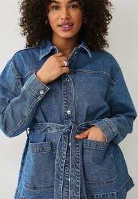 Denim jacket in gradient blauw met lange mouwen, knoopsluiting, twee voorzakken en een gebonden taille. Heeft een kraag en een zachte textuur.