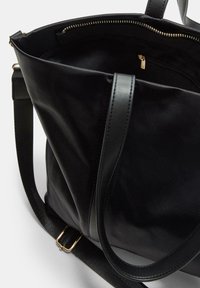 Schwarze Leder-Shopper-Tasche mit einem Hauptfach mit Reißverschluss, verstellbarem Riemen und goldfarbenen Metallakzenten. Glatte Textur und schlichtes Design.