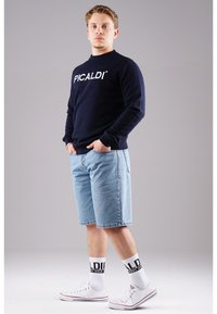 Navy sweatshirt with "PICALDI" logo, denim shorts, white high-top shoes, and crew socks with black branding. Casual outfit in a neutral setting.