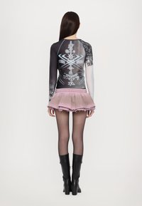 Long-sleeve mesh top with graphic patterns in black and blue, paired with a light pink, layered, ruffled skirt and knee-high black leather boots.
