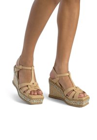 Sandali con zeppa beige con cinturini incrociati, dotati di una piattaforma intrecciata testurizzata e un accento decorativo di perline lungo la base.