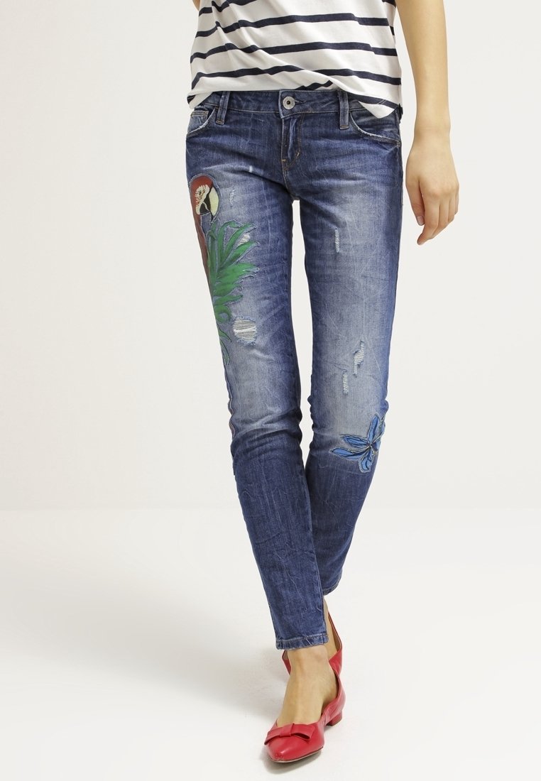 Vaqueros de mezclilla en azul oscuro con detalles desgastados y bordados coloridos de un loro y diseños florales en la parte frontal, ajustados al cuerpo.