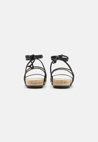 Sandales noires en cuir avec des brides, dotées de semelles en jute tressé, affichant une base plate et des lacets en ruban noués à l'arrière pour un ajustement.