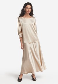 Beige satin topp med rund halsringning och trekvartslånga ärmar, kombinerad med en lång, flödande kjol; slät textur och elegant silhuett.