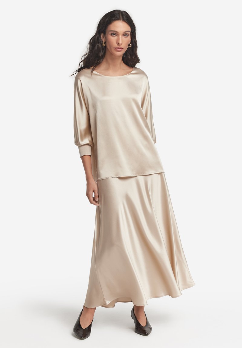 Beige satin topp med rund halsringning och trekvartslånga ärmar, kombinerad med en lång, flödande kjol; slät textur och elegant silhuett.