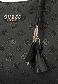Borsa nera con motivo logo in rilievo, dettagli in metallo dorato e frange decorative. Texture liscia con una forma strutturata.