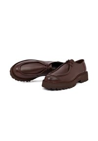 Scarpe in pelle marrone con punta arrotondata, dettagli di cucitura minimi e suola in gomma spessa e decorata. Lacci integrati nel design.