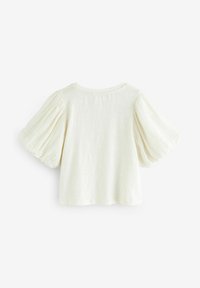 Haut crème avec des manches courtes et bouffantes et un col rond. Fabriqué en tissu texturé ; design simple et épuré sans détails supplémentaires.