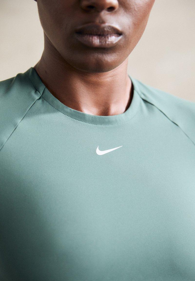 Maglia atletica verde Nike concollo rotondo, texture liscia e logo bianco sul petto, caratterizzata da maniche raglan eleganti.