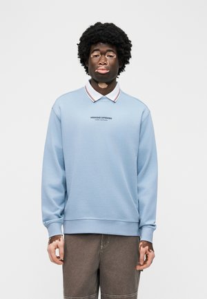 Νέος με λεύκη φοράει μπλε φούτερ με το κείμενο «Weekend Offender Admit Nothing», στέκεται μπροστά σε απλό λευκό φόντο.