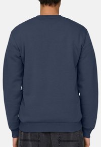 Felpa blu navy con collo rotondo, maniche lunghe, polsi e fondo a coste. Il materiale ha una consistenza liscia e un design minimalista.