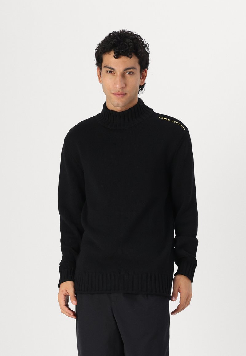 Μαύρο ζιβάγκο πουλόβερ με ριχτές μανσέτες και στρίφωμα, με χρυσές λεπτομέρειες κειμένου στον αριστερό ώμο. Μαλακή πλεκτή υφή.