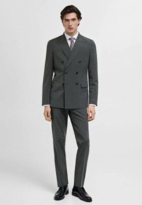 Costum gri cu două rânduri de nasturi, cu o croială ajustată, rever cu tăietură oblică, nasturi negri și pantaloni gri asortați. Se asortează cu o cămașă deschisă și o cravată.