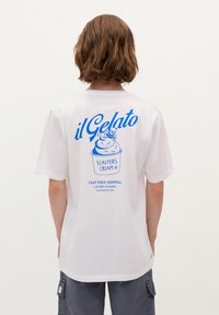 Weißes Baumwoll-T-Shirt mit blauer Grafikschrift und Illustration von Gelato auf dem Rücken. Kurze Ärmel und lässige Passform.