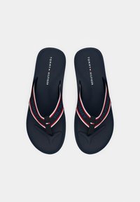 Navy blue flip-flops with a textured sole. Features black and red straps with "TOMMY" and "HILFIGER" branding. Clean design, lightweight material.