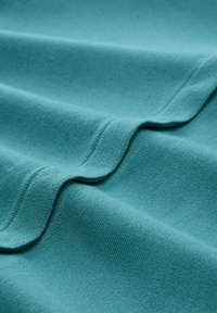 Tkanina w kolorze morskim o gładkiej fakturze, z delikatnym prążkowaniem i falistym brzegiem. Materiał wygląda na miękki i elastyczny.