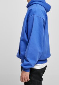 Sudadera con capucha azul de algodón con un bolsillo delantero tipo canguro, puños y dobladillo acanalados, y un ajuste holgado. Cuenta con capucha con cordón y textura suave.