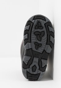 Semelle de chaussure en caoutchouc noir avec un motif de bande de roulement texturé multidirectionnel, présentant des rainures et des reliefs pour l'adhérence.