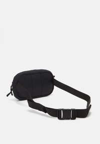 Bolsa de cintura preta em tecido, com um exterior texturizado e fluffy. Apresenta uma parte frontal suave e acolchoada, uma alça ajustável e fecho de fivela.