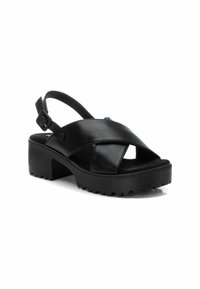 Sandalia de cuero negro con diseño de tiras cruzadas, correa de talón ajustable y suela de goma texturizada. Punta cuadrada y tacón ligeramente elevado.