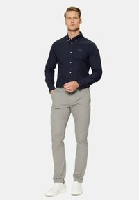 Camicia navy con bottoni e maniche lunghe, pantaloni grigi slim-fit e sneakers bianche, esposti su uno sfondo neutro.
