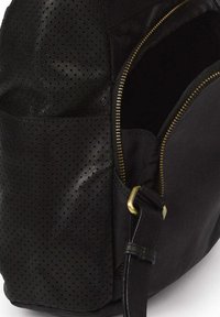 Zwarte leren tas met geperforeerde textuur, ritssluiting en goudkleurige hardware. Bevat een zijriem en een gladde body.
