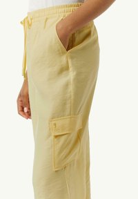 Helle gelbe Cargo-Hosen mit elastischem Bund, seitlicher Tasche und einer aufgesetzten Tasche am Bein. Glatte Textur, lockere Passform.